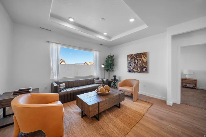 Recessed lighting, tray ceiling, large picture window, wood-finish flooring, and white walls