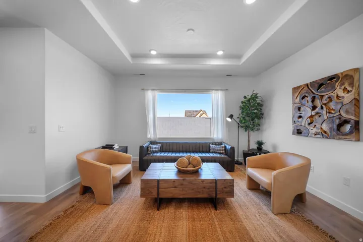 Recessed ceiling lighting, tray ceiling, hard surface flooring, white walls, and a window with natural light