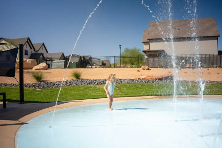 Splash pad with integrated water features, surrounded by green space, and a protective shade structure