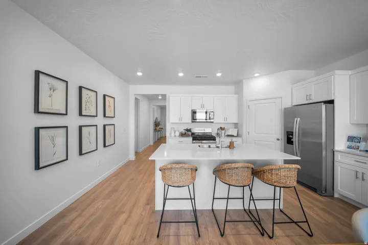 Kitchen featuring an island with seating, white cabinetry, stainless steel appliances, and wood-finish flooring