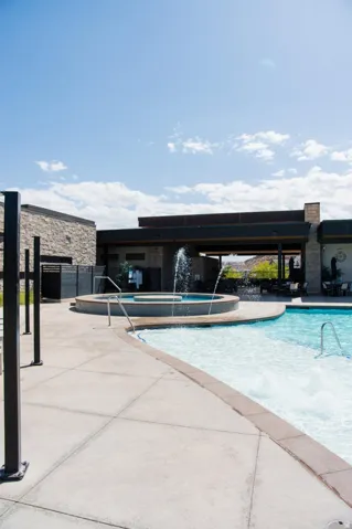 Swimming pool with integrated spa and water features, adjacent to a stone-clad structure with an open-air area