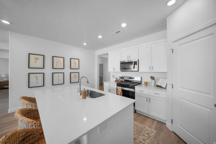 Kitchen featuring white cabinetry, stainless steel appliances, a center island with an undermount sink, and recessed lighting