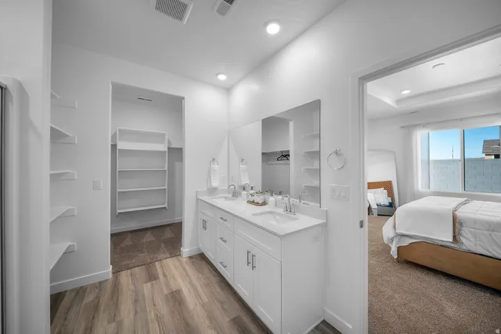Dual vanity with undermount sinks and white cabinetry, wood-finish flooring, recessed lighting, and built-in shelving