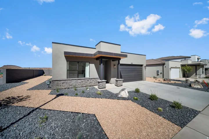 Modern stucco exterior with stone accents, xeriscape landscaping, an integrated garage, and a covered entry