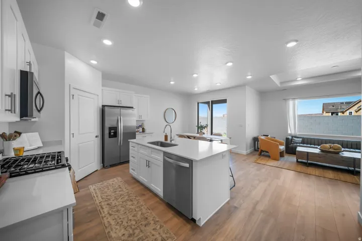 Open-concept living space with wood-finish flooring, recessed lighting, and a kitchen island featuring a sink