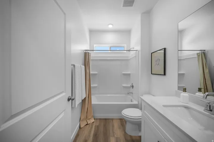 Wood-finish flooring with a white vanity featuring an integrated sink, polished chrome faucet, and a large wall-mounted mirror