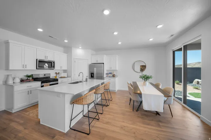 White cabinetry, stainless steel appliances, wood-finish flooring, recessed lighting, and a sliding glass door