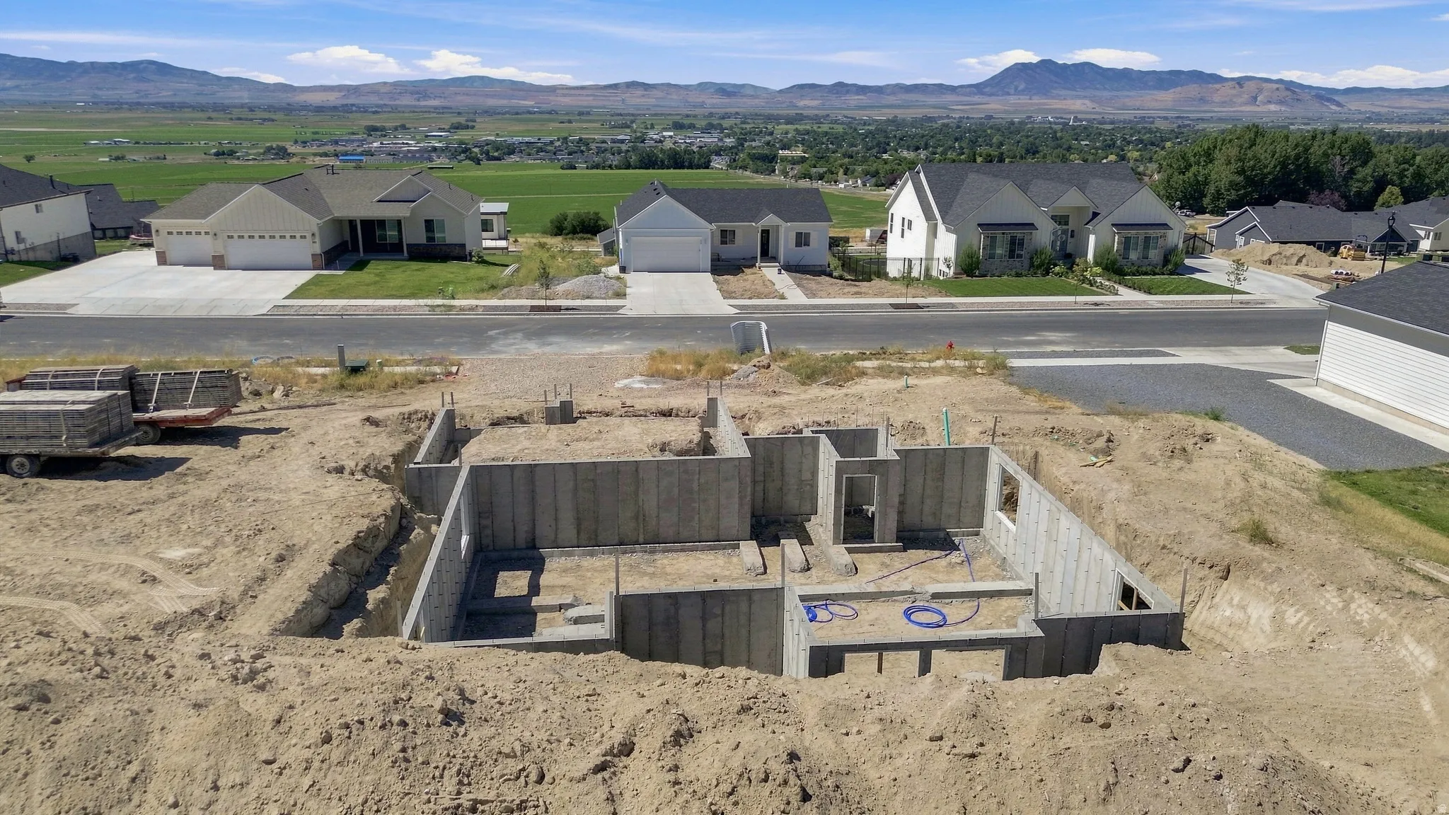 Concrete foundation with excavated earth, surrounded by developed residential properties, with distant mountains