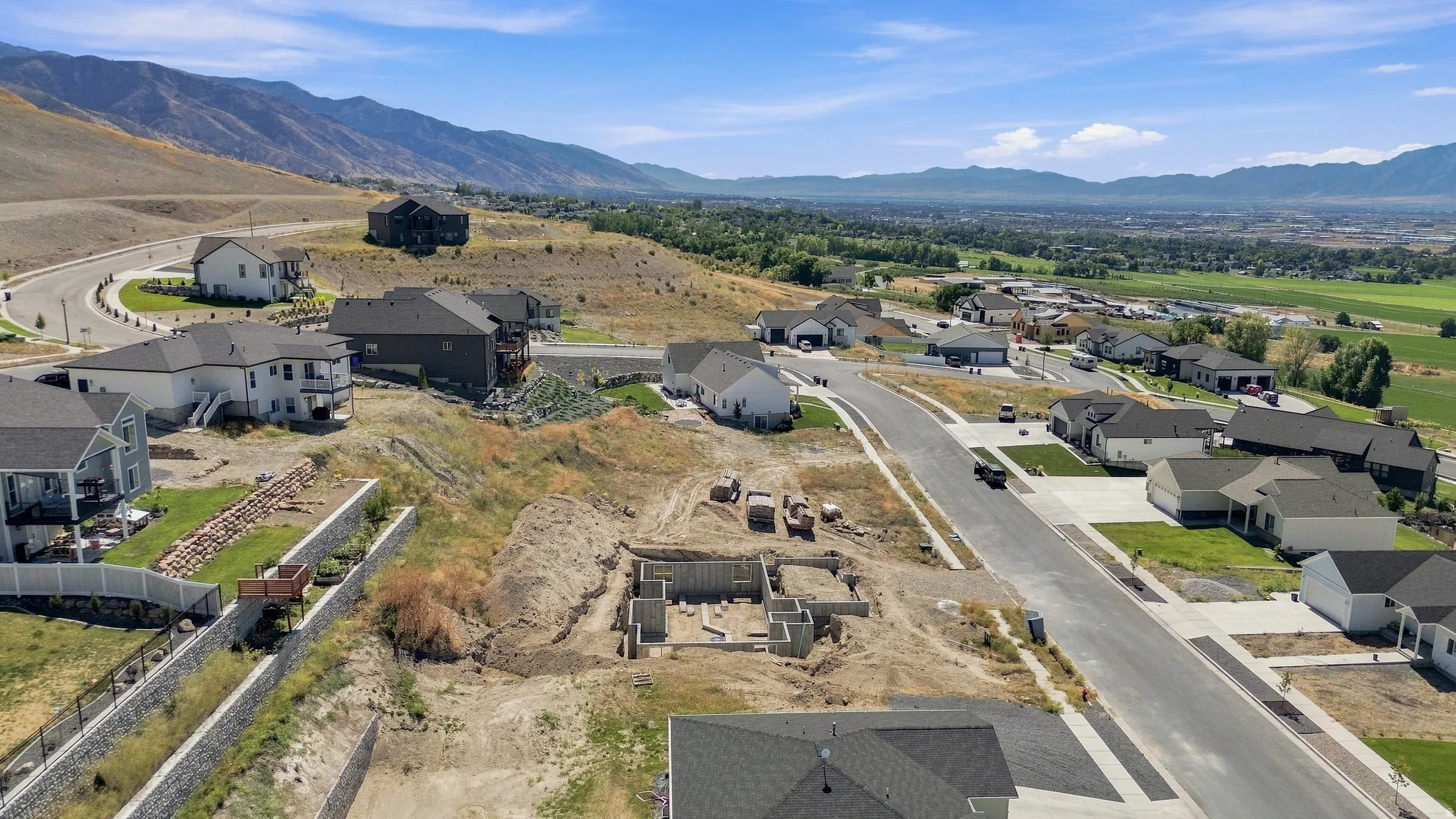 Mountainous terrain backdrop, residential development, paved roadways, established landscaping, and building foundations