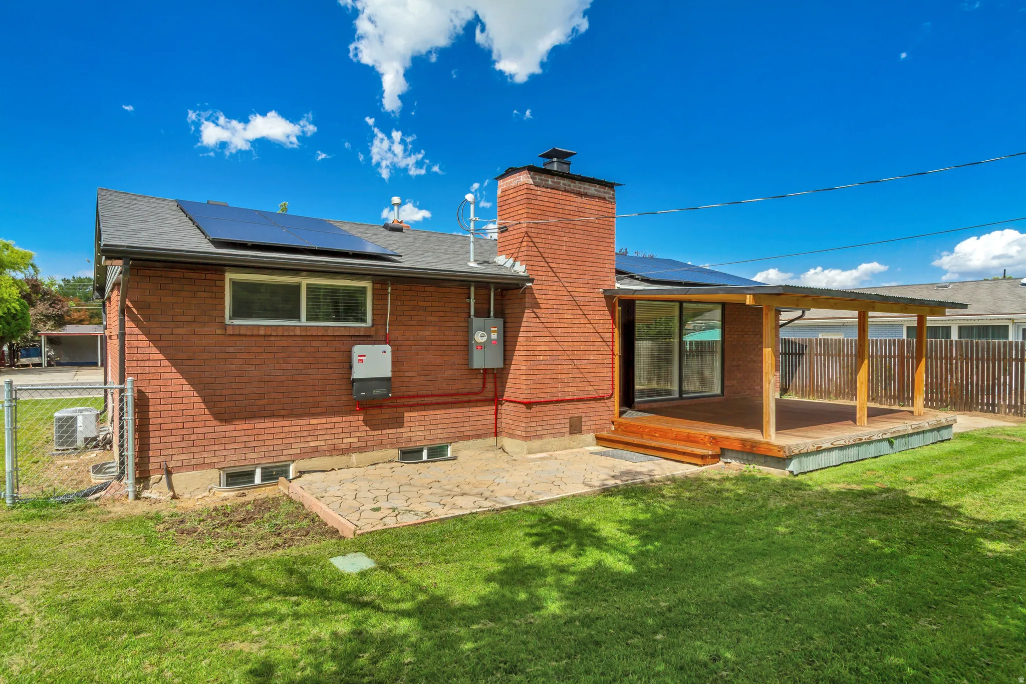 Brick exterior featuring a covered wood deck, sliding glass door, solar panels, and full fencing