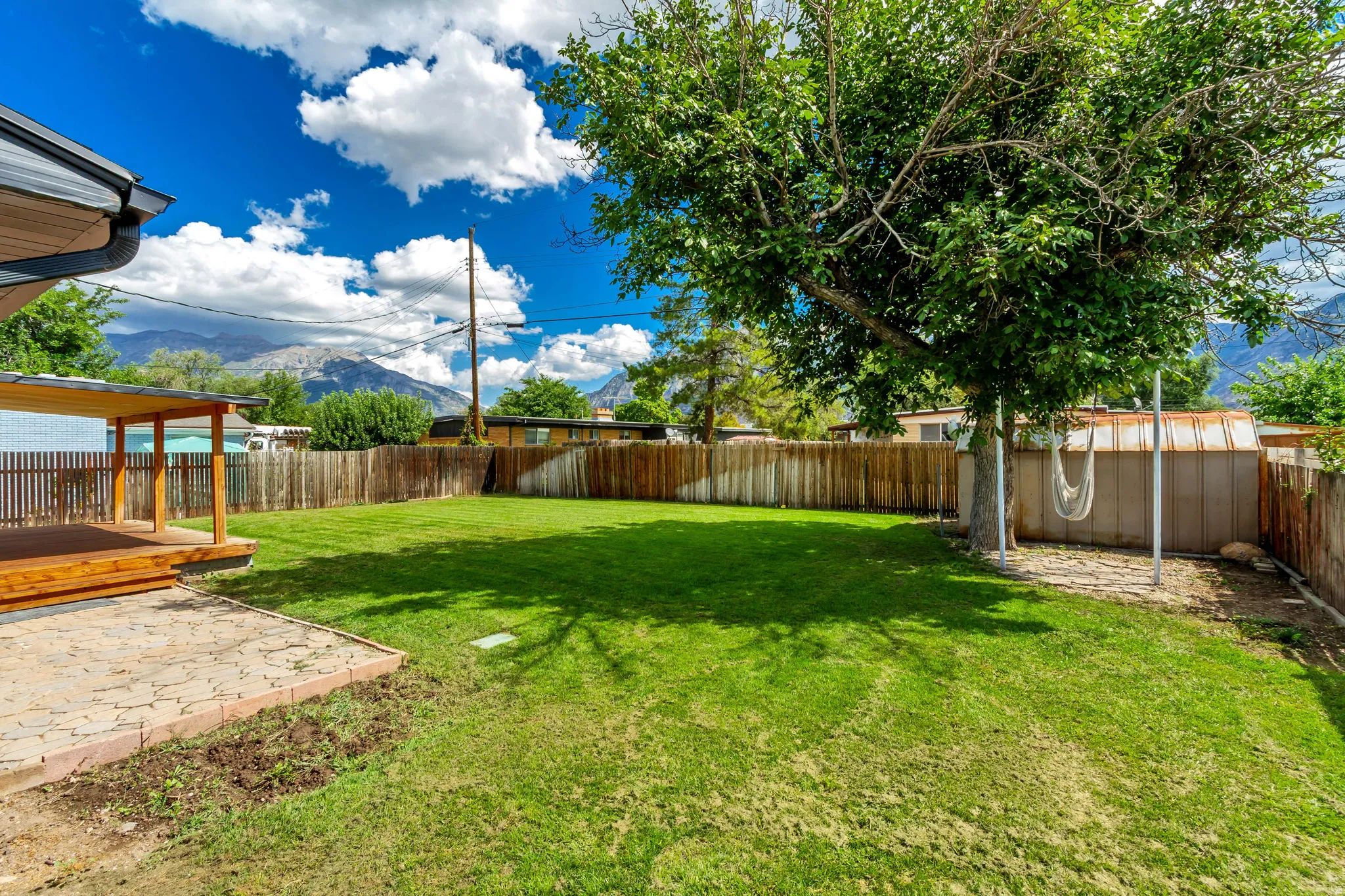 Spacious lawn area with mature trees, a covered patio, and a stone-paver patio