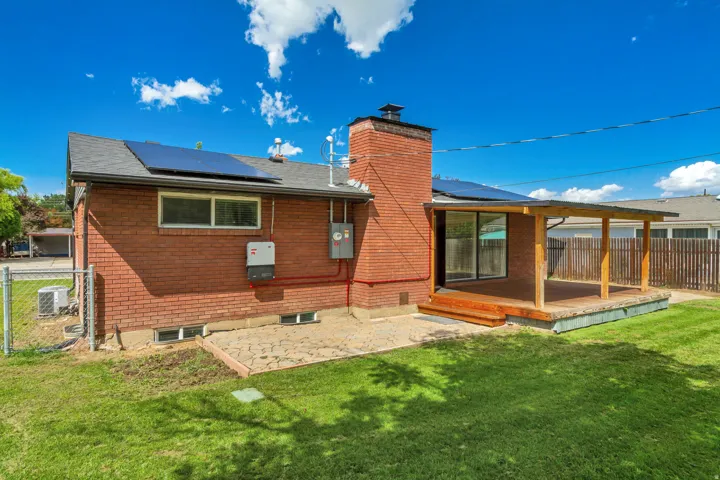 Brick exterior featuring a covered wood deck, sliding glass door, solar panels, and full fencing