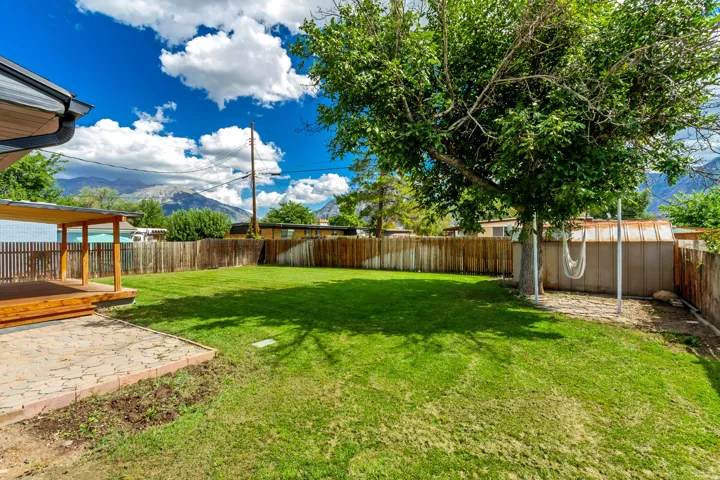 Spacious lawn area with mature trees, a covered patio, and a stone-paver patio