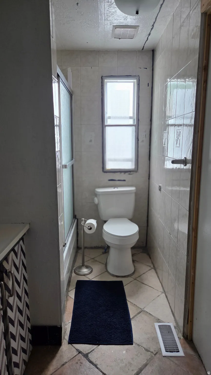 Bathroom featuring a white toilet, tiled walls, and a window