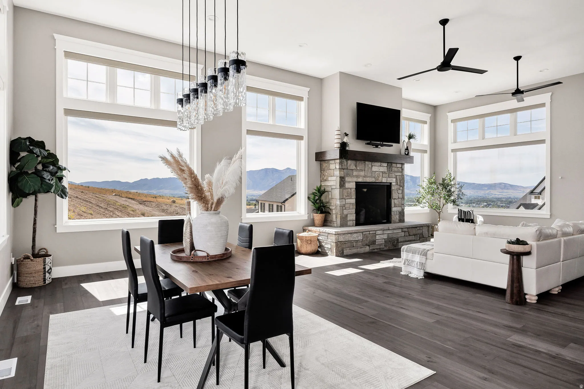 Spacious room featuring multiple large windows, wood-finish flooring, a stone-clad fireplace with a wood mantle, and a linear chandelier