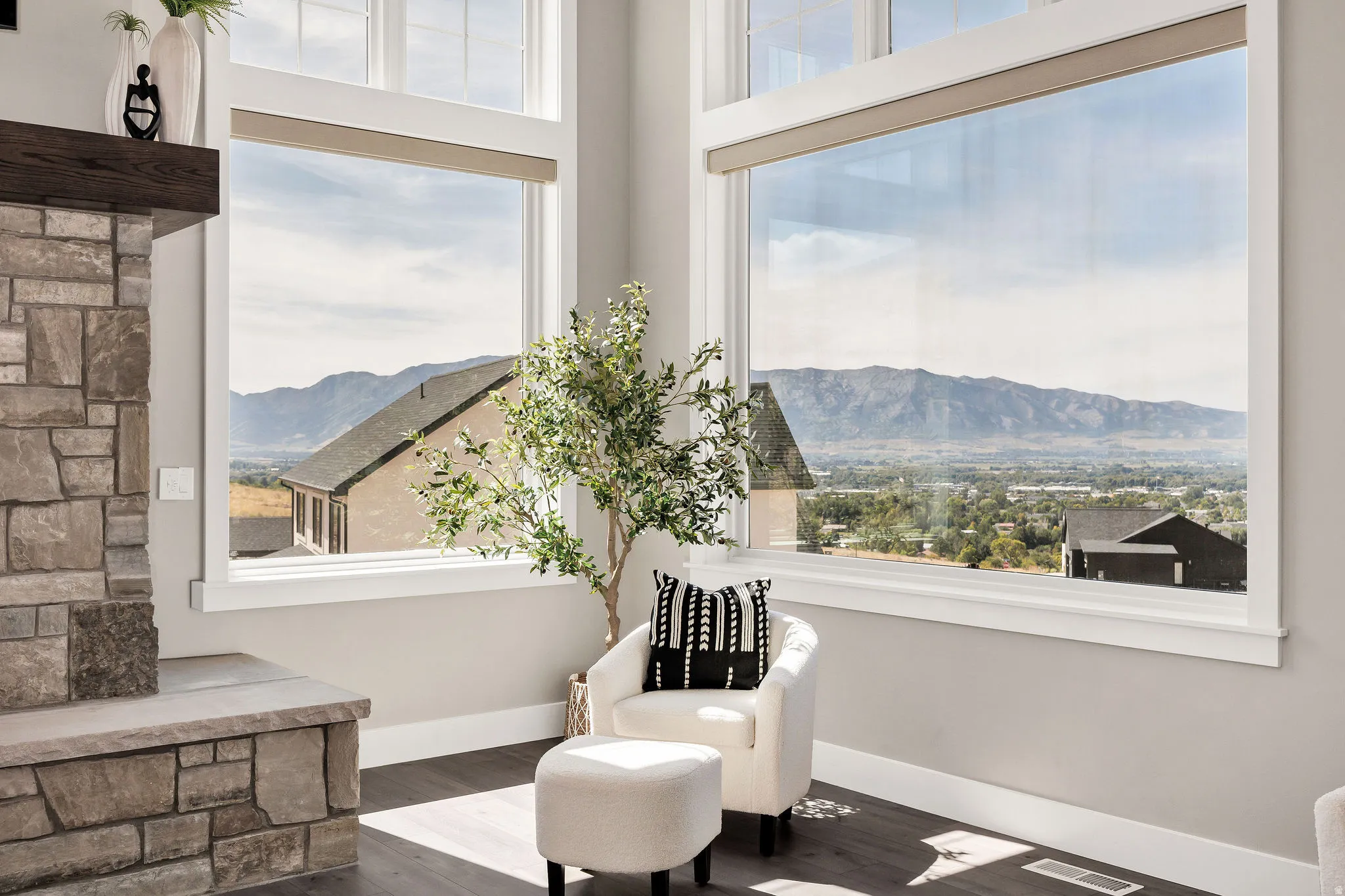 Expansive windows showcasing mountain scenery, stone-clad fireplace with wood mantle, and wood-finish flooring