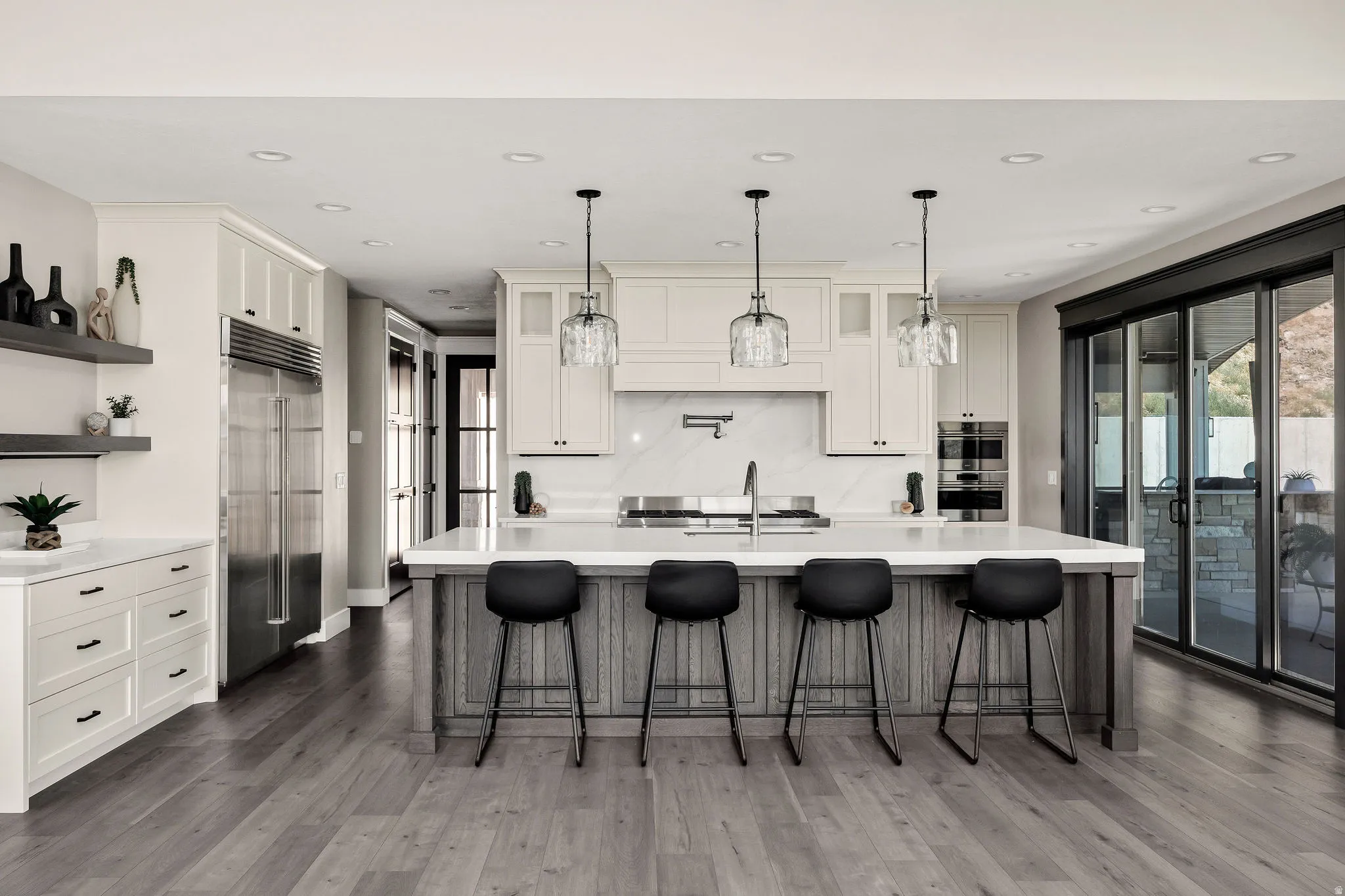 Gourmet kitchen with wood-finish flooring, a large center island, built-in stainless steel appliances, white cabinetry, and sliding glass doors