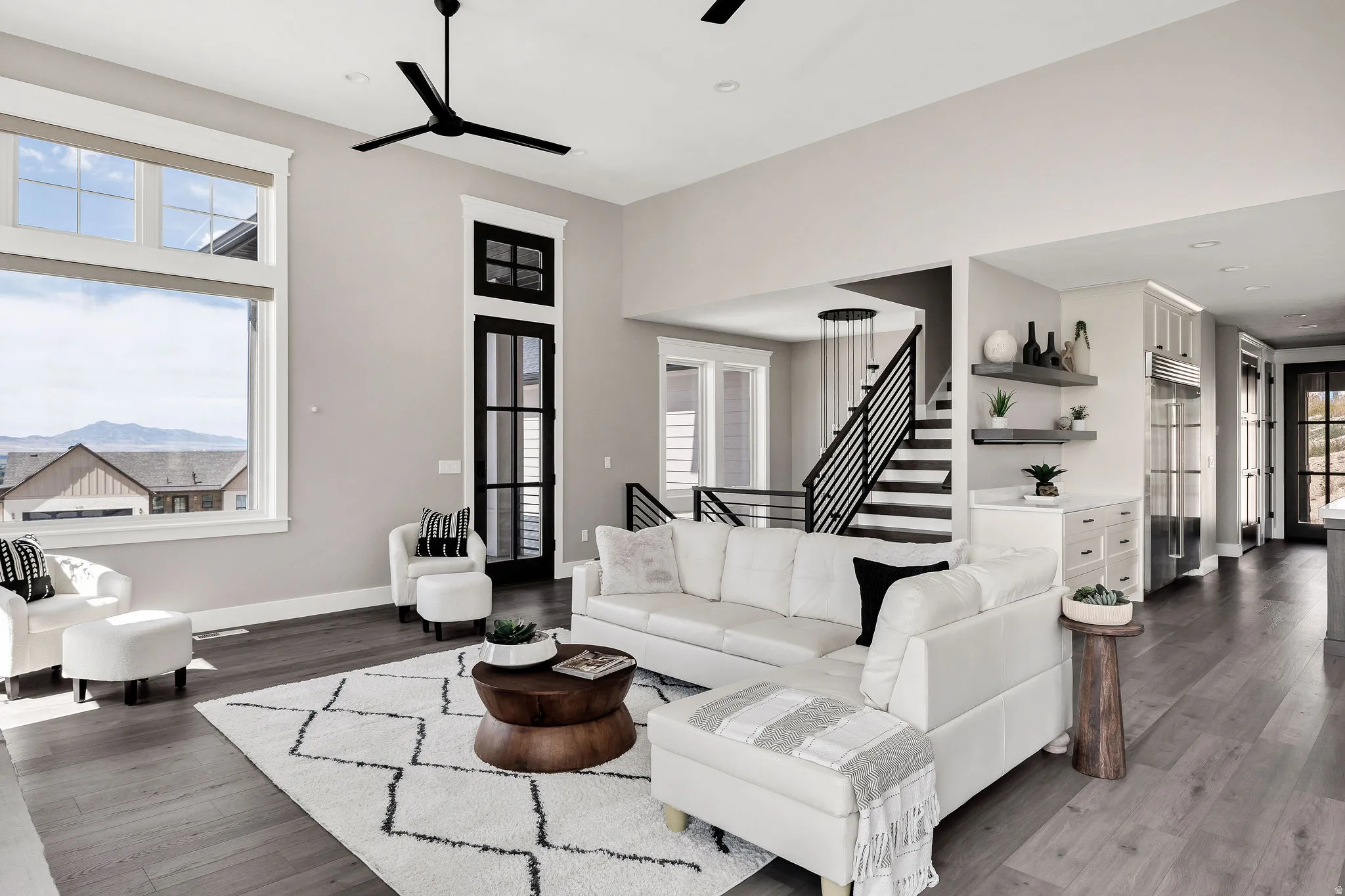 Open concept living area featuring high ceilings, wood-finish flooring, a modern staircase with metal railings, and integrated shelving with lower cabinetry