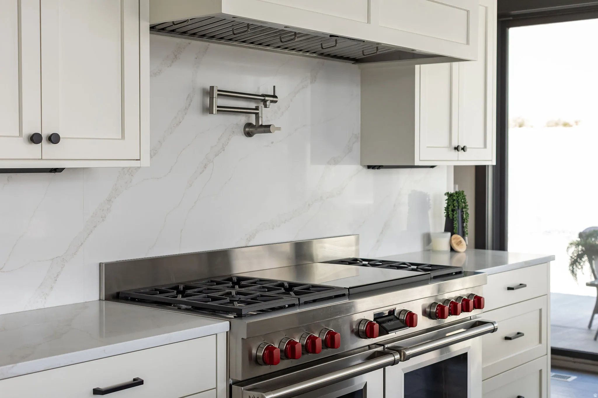Professional-grade stainless steel range with red accents, full-height veined backsplash, pot filler, custom cabinetry with matte black hardware, and an integrated range hood