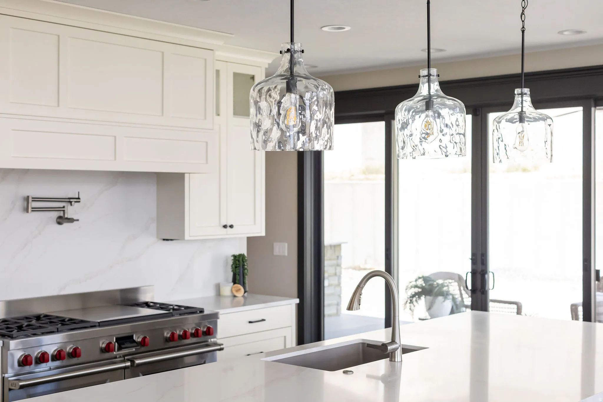 White cabinetry with crown molding, stainless steel range, white countertop with integrated sink, contemporary pendant lighting, and dark-framed sliding glass doors