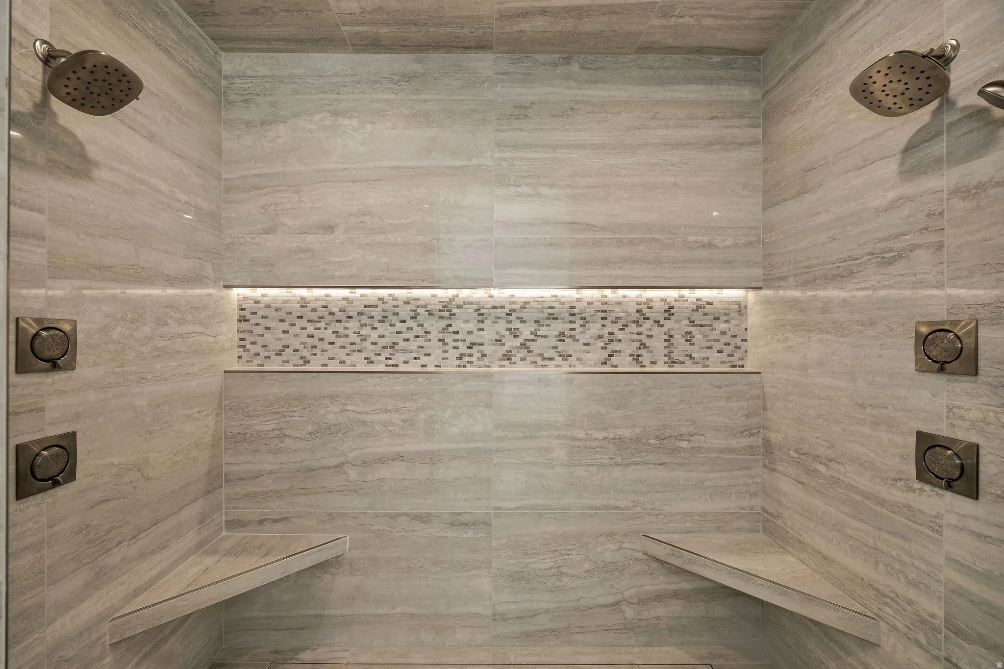 Shower with dual rain shower heads, integrated benches, tiled walls, and mosaic tile accent