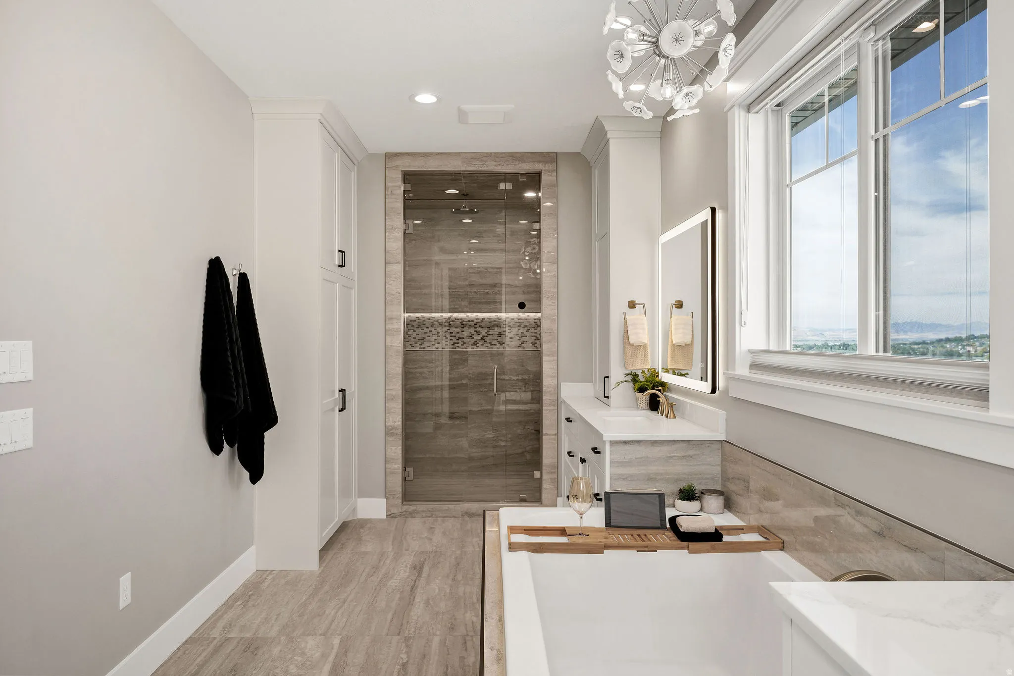Freestanding tub, glass-enclosed shower, built-in cabinetry, dual-sink vanity with quartz countertop, and large window with exterior scenery