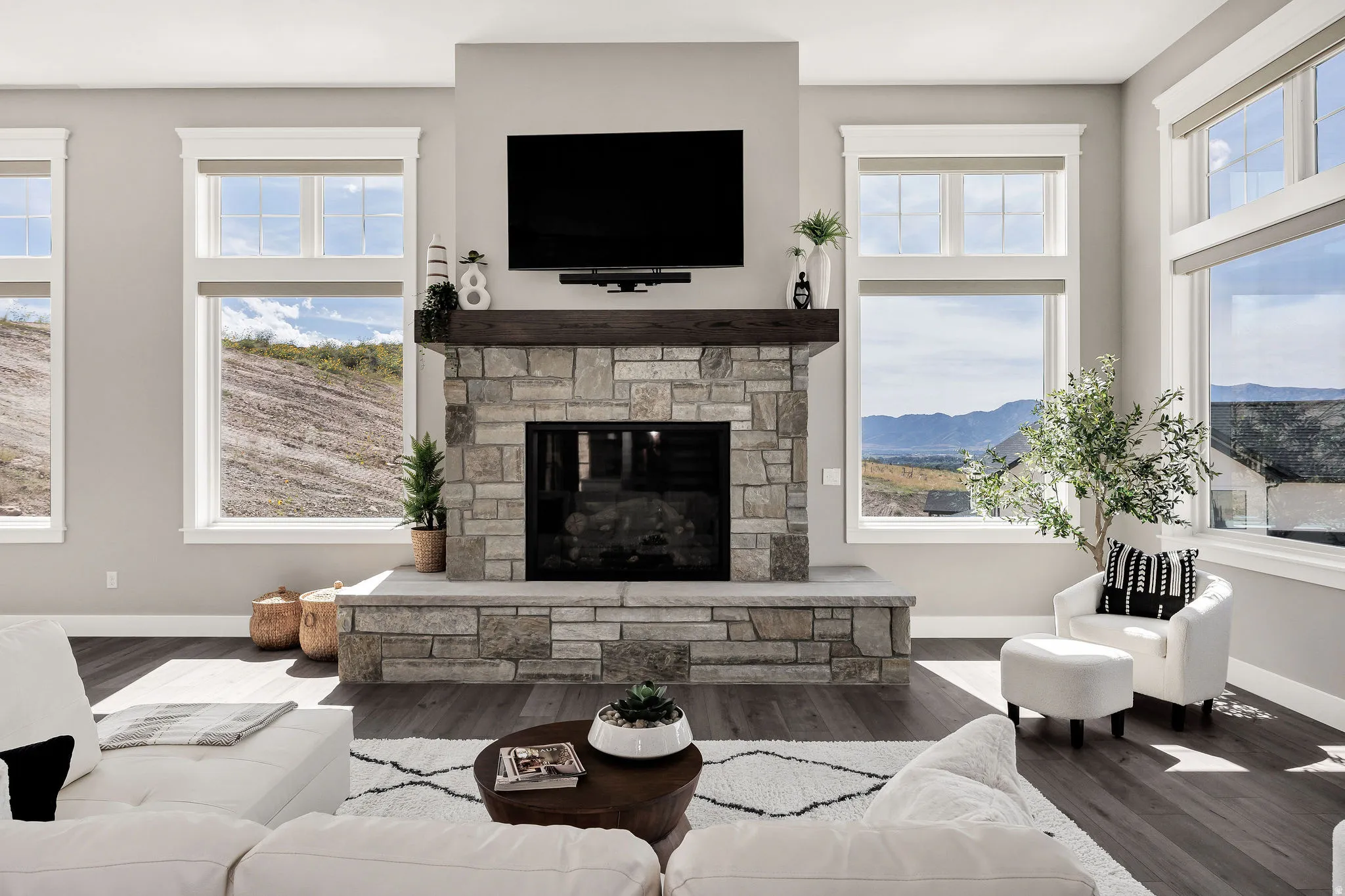 Stone-clad fireplace with hearth, wood-finish flooring, and expansive windows