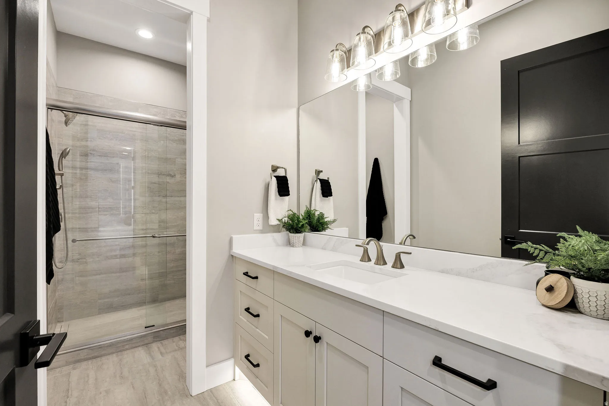 Bathroom featuring an expansive vanity with double sinks and a large mirror, a glass-enclosed shower with tiled walls, and recessed lighting