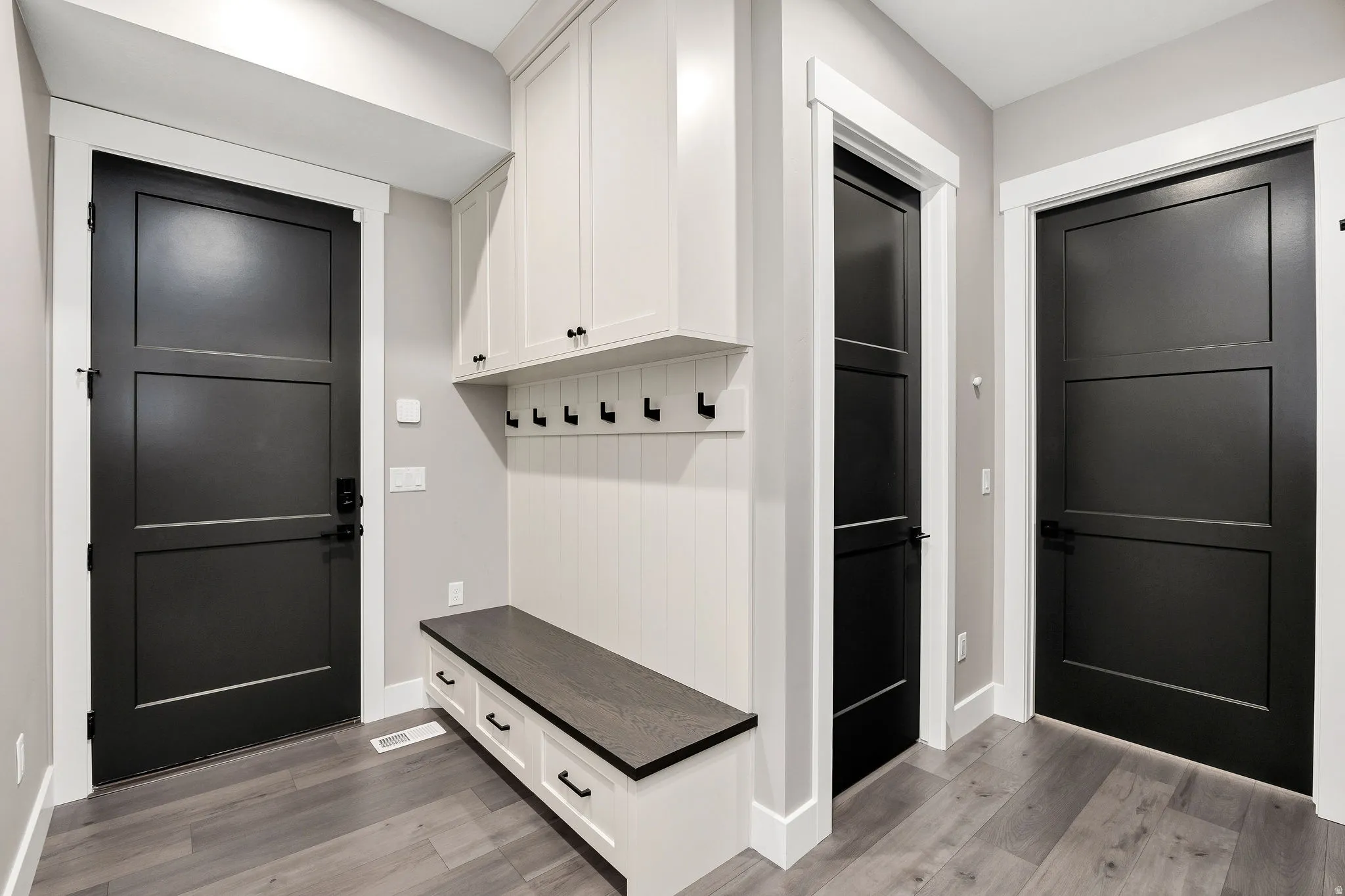 Built-in bench with storage drawers, overhead cabinetry, wall-mounted coat hooks, and wood-finish flooring