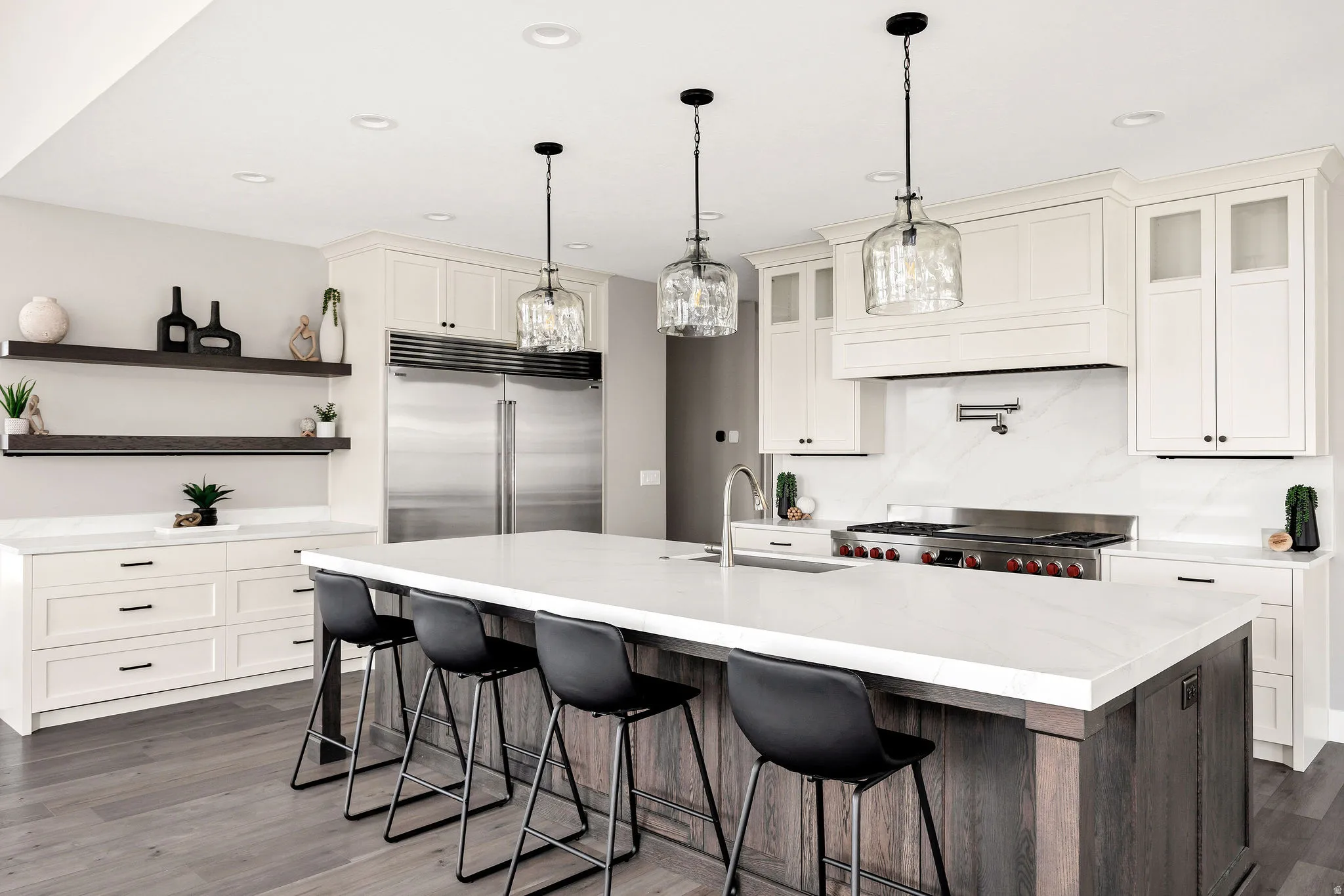 Expansive kitchen featuring a large central island with seating, stainless steel appliances, white cabinetry with varied door styles, and wood-finish flooring