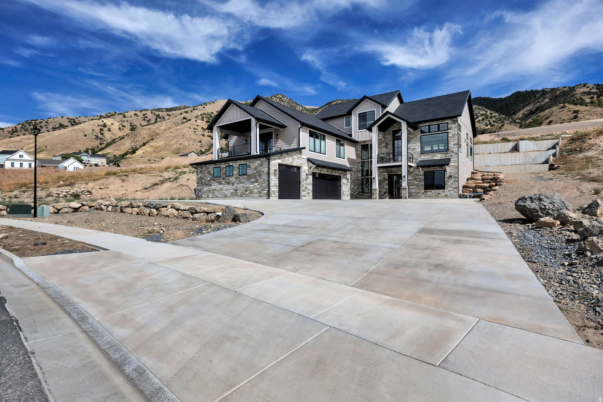 Stone and siding exterior with a multi-level design, multiple attached garages, a concrete driveway, and a retaining wall