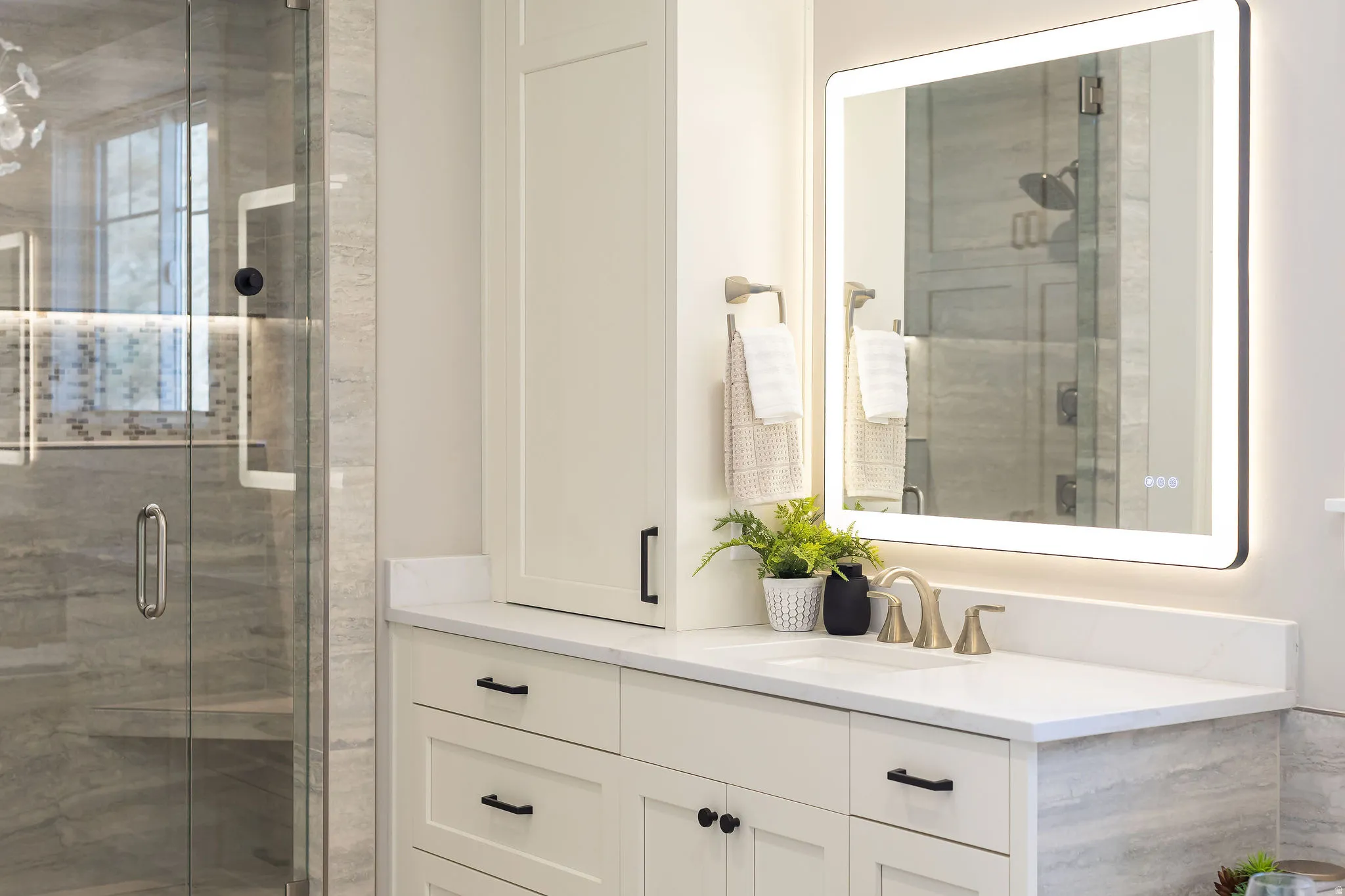 Backlit mirror, undermount sink, quartz countertop, shaker-style cabinetry, and glass-enclosed shower