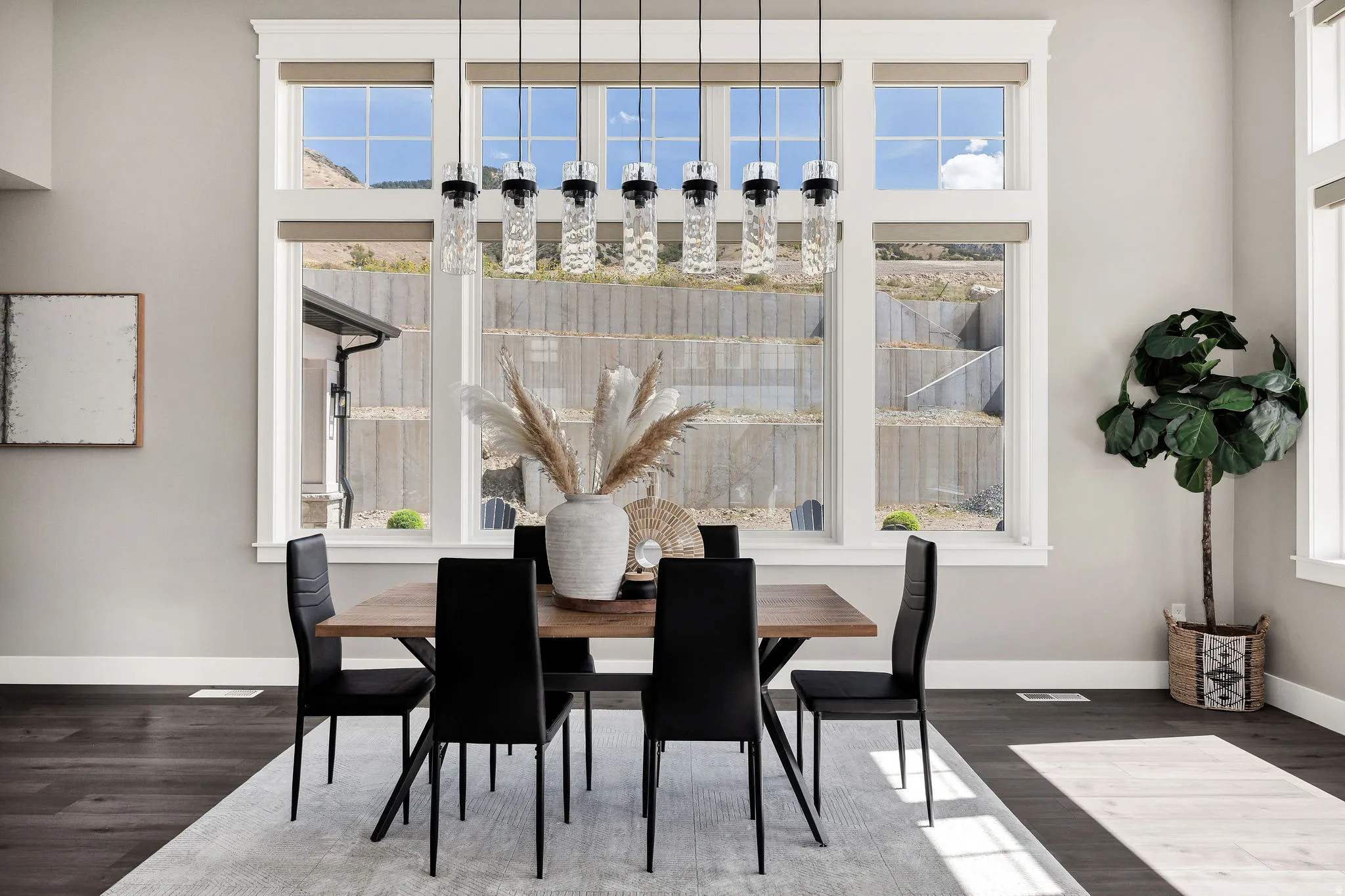 Expansive window array, contemporary chandelier with multiple pendants, rich wood-finish flooring, and neutral wall tones