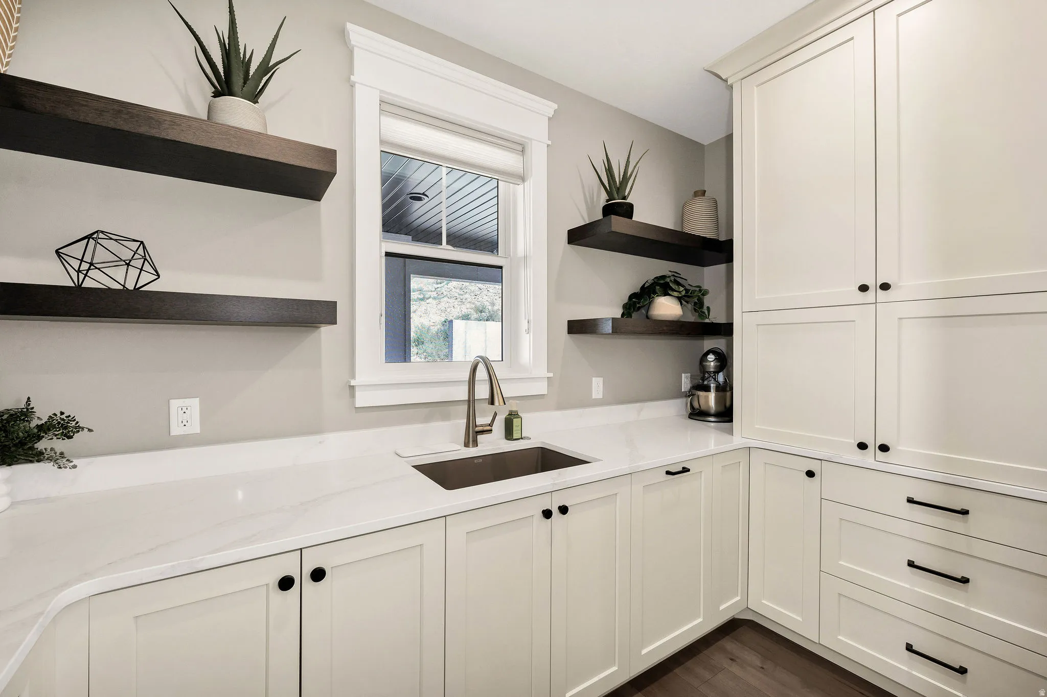 White shaker-style cabinetry with matte black hardware, white countertops, stainless steel sink with a gooseneck faucet, dark wood-finish open shelving, and dark wood-finish flooring