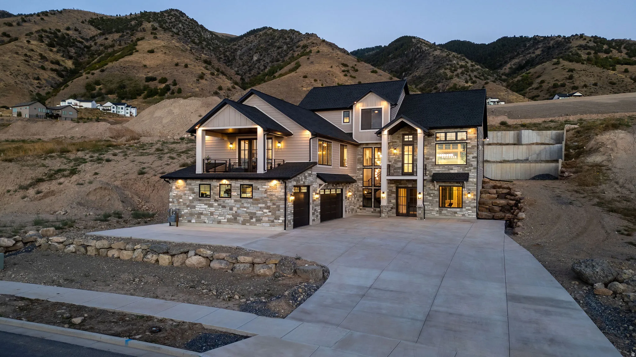 Two-story residence featuring stone and siding exterior, multi-car concrete driveway, and covered balcony