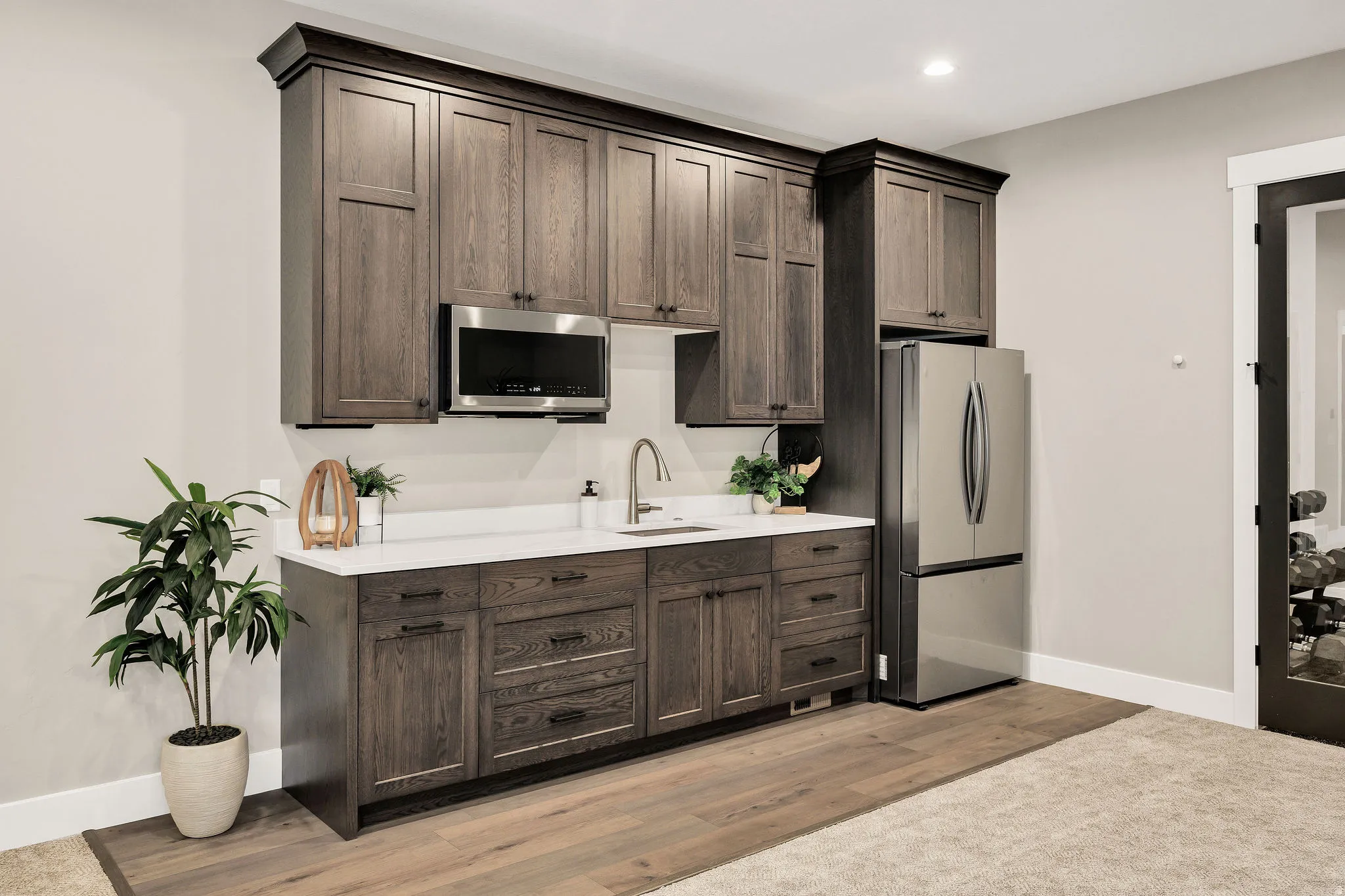 Built-in cabinetry with dark wood finish, stainless steel microwave, white countertop, stainless steel sink with gooseneck faucet, and stainless steel refrigerator