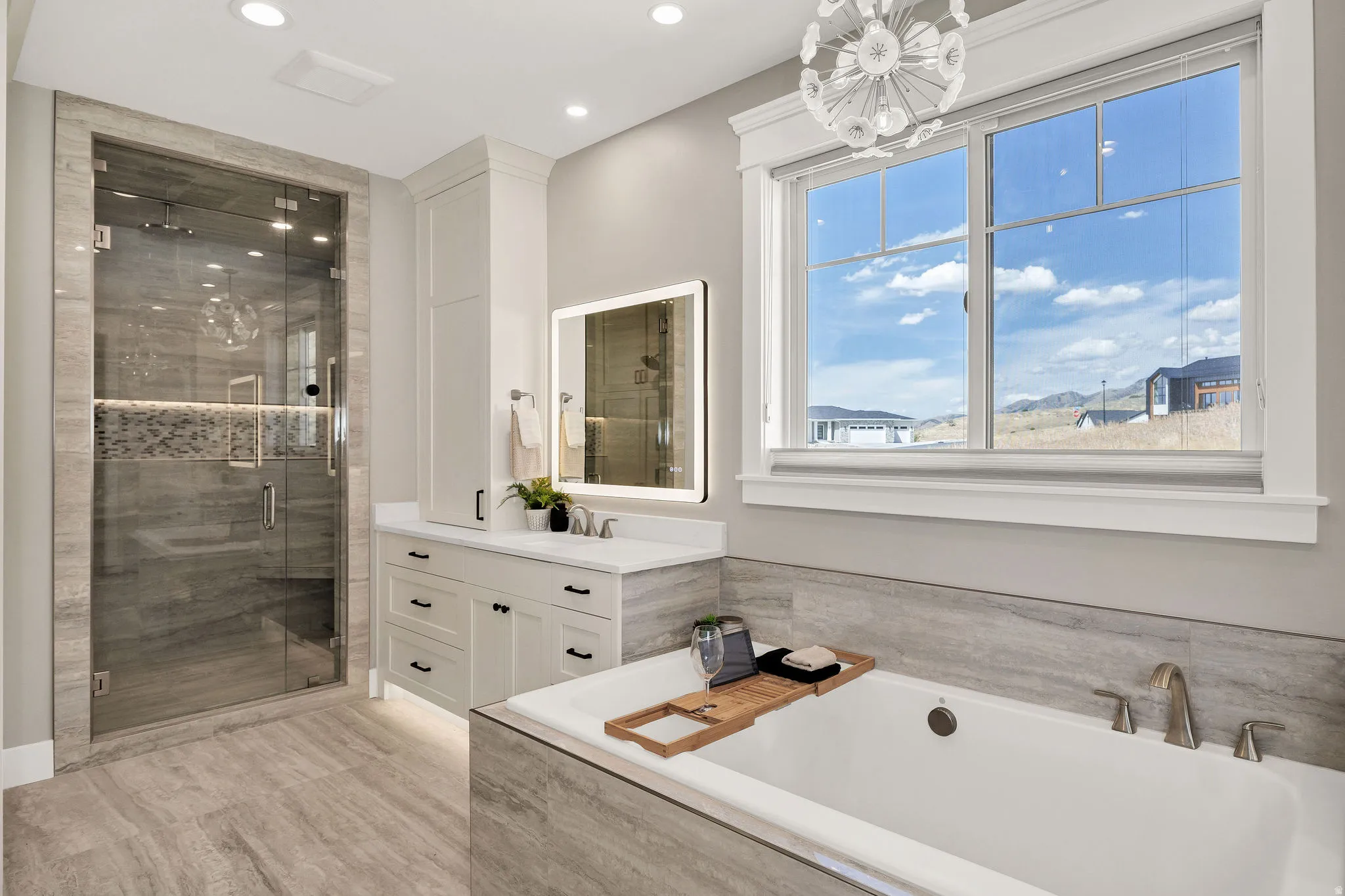Glass-enclosed shower with tiled surround, white vanity with integrated sink, freestanding soaking tub with deck-mounted faucet, large multi-pane window, and recessed lighting