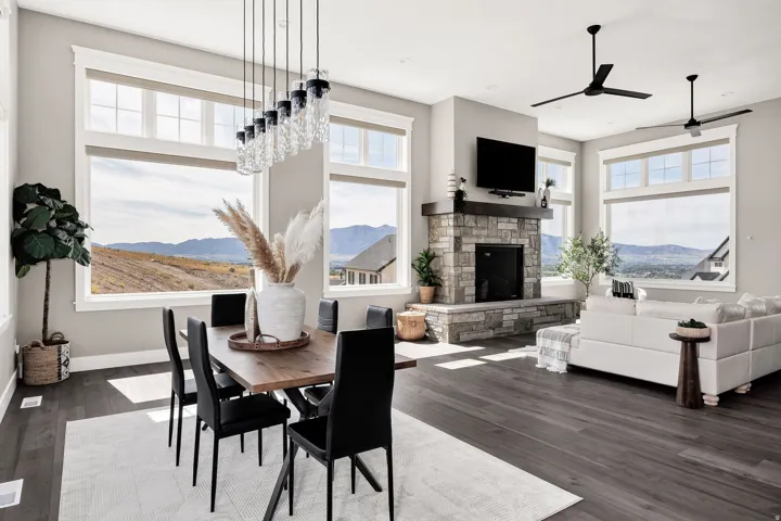 Spacious room featuring multiple large windows, wood-finish flooring, a stone-clad fireplace with a wood mantle, and a linear chandelier