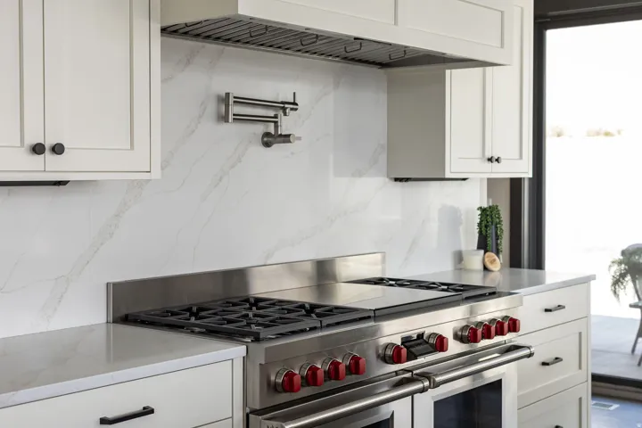 Professional-grade stainless steel range with red accents, full-height veined backsplash, pot filler, custom cabinetry with matte black hardware, and an integrated range hood