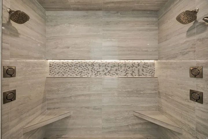 Shower with dual rain shower heads, integrated benches, tiled walls, and mosaic tile accent