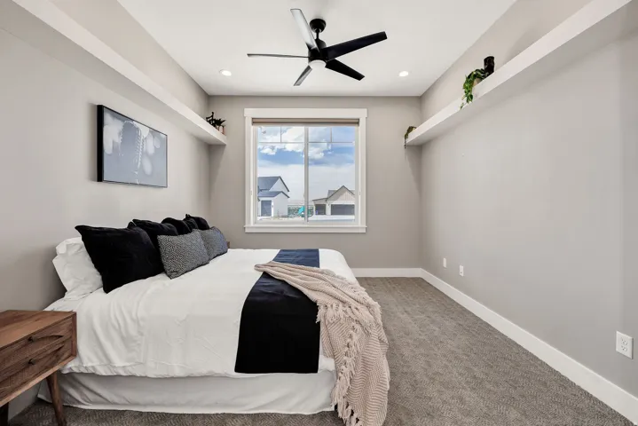 Recessed lighting, ceiling fan, window with white trim, wall-mounted display shelves, and carpeted flooring
