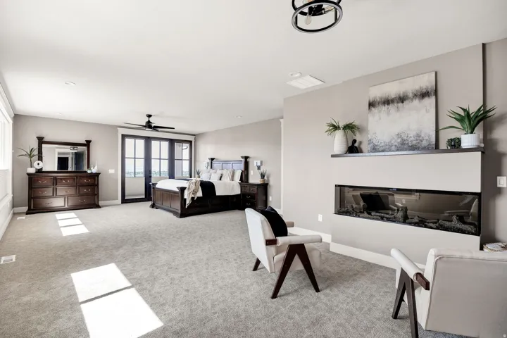 Spacious room featuring a linear fireplace, black framed glass double doors, light gray carpeting, and a ceiling fan