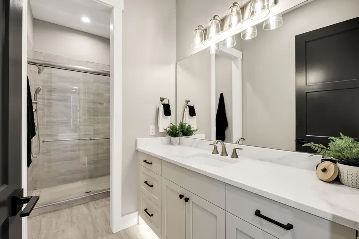 Bathroom featuring an expansive vanity with double sinks and a large mirror, a glass-enclosed shower with tiled walls, and recessed lighting