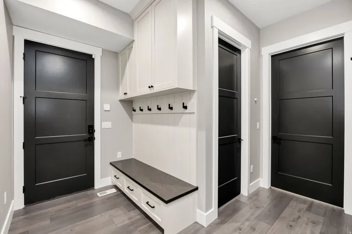 Built-in bench with storage drawers, overhead cabinetry, wall-mounted coat hooks, and wood-finish flooring