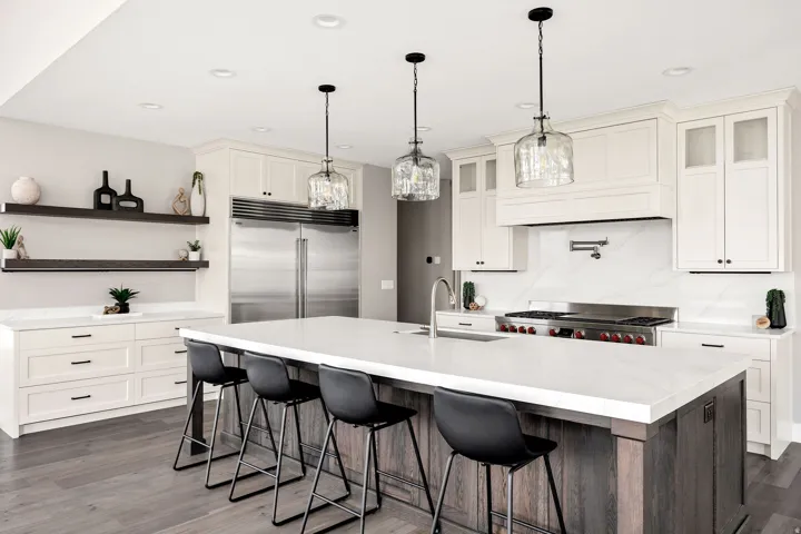 Expansive kitchen featuring a large central island with seating, stainless steel appliances, white cabinetry with varied door styles, and wood-finish flooring