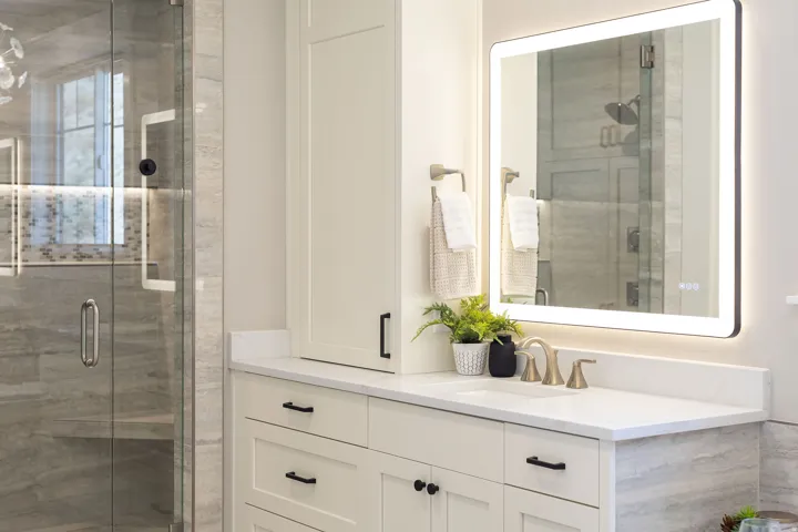 Backlit mirror, undermount sink, quartz countertop, shaker-style cabinetry, and glass-enclosed shower
