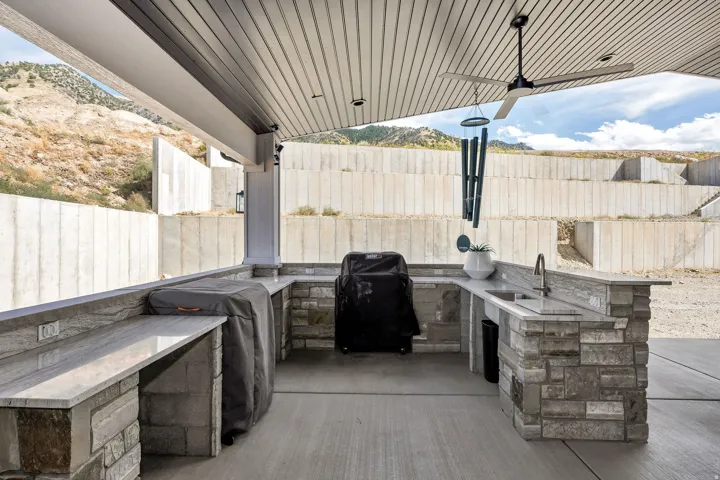 Outdoor kitchen featuring stone-clad cabinetry, a built-in sink with a gooseneck faucet, an expansive counter, and a ceiling fan