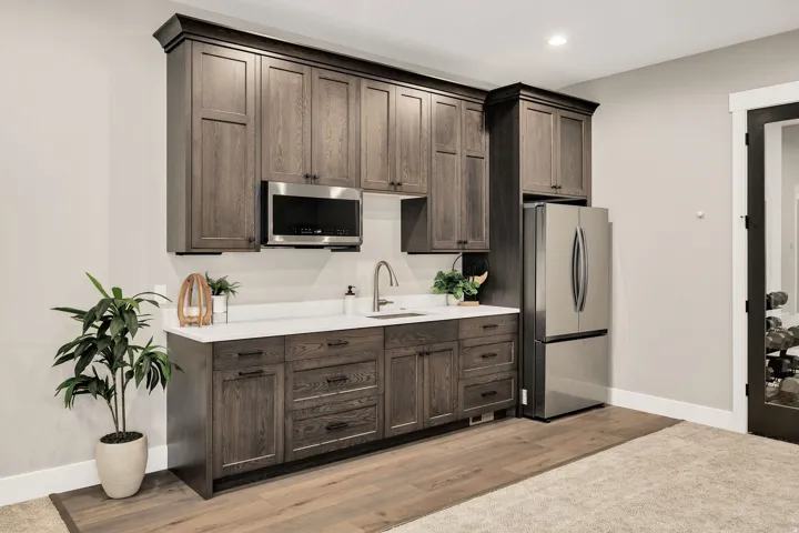 Built-in cabinetry with dark wood finish, stainless steel microwave, white countertop, stainless steel sink with gooseneck faucet, and stainless steel refrigerator