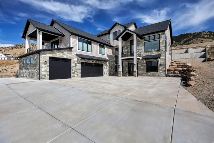 Modern exterior with stone and siding facade, multiple attached garages, a concrete driveway, and prominent entry