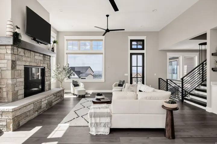 Open-concept living space anchored by a stone fireplace with a black insert, dark wood-finish flooring throughout, and abundant natural light from oversized windows